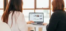 two women talking while looking at laptop computer