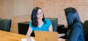 woman in teal t-shirt sitting beside woman in suit jacket